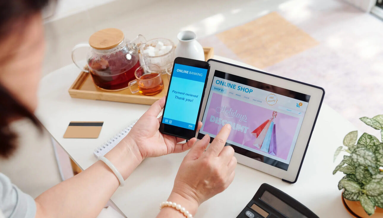 woman holding mobile phone beside dablet on office table for Top 11 Best Shopify Apps to Improve Conversion Rate