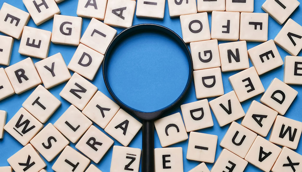A magnifying glass surrounded by scrabble tiles.