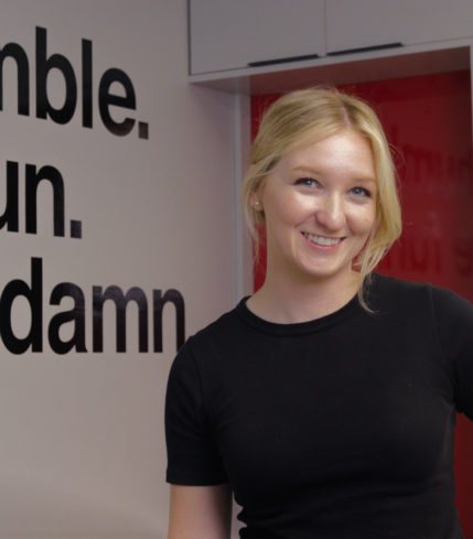 ready artwork marketing agency los angeles team member felicity porter smiling while standing in monrovia office beside wall art core values for be humble, have gun, give a damn