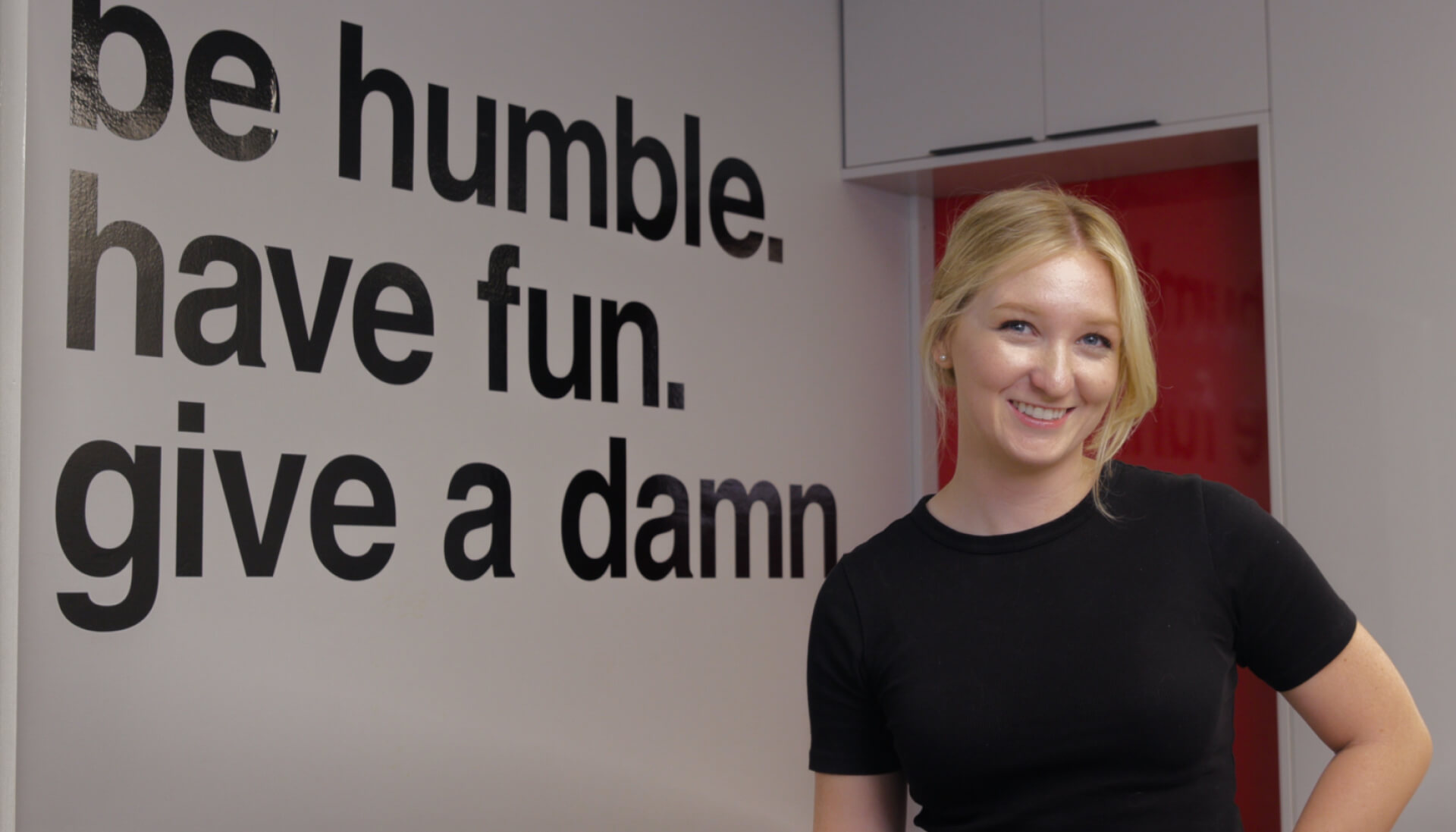 ready artwork marketing agency los angeles team member felicity porter smiling while standing in monrovia office beside wall art core values for be humble, have gun, give a damn